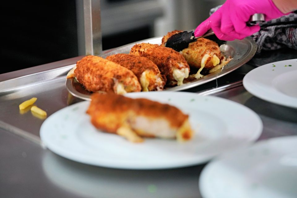 Gekochtes Cordon Bleu wird mit rosa behandschuhten Händen und Zangen auf den Tellern serviert, neben leeren weißen Tellern.