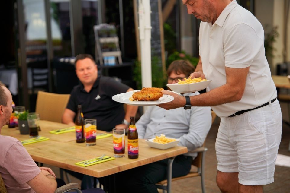 Kellner serviert einer Gruppe an einem Restauranttisch im Freien Schnitzel und Pommes.