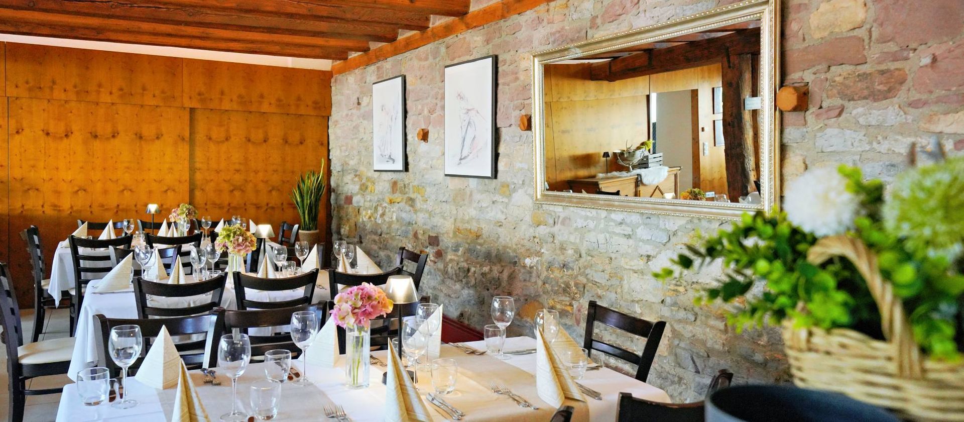 Innenansicht eines Restaurants mit gedeckten Tischen, Steinwänden und gerahmter Kunst.