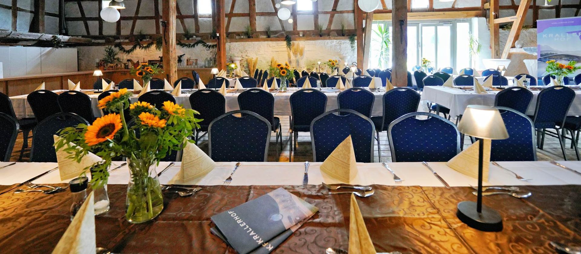 Ein Bankettsaal mit für eine formelle Veranstaltung gedeckten Tischen, Sonnenblumen und einem Scheinwerfer.
