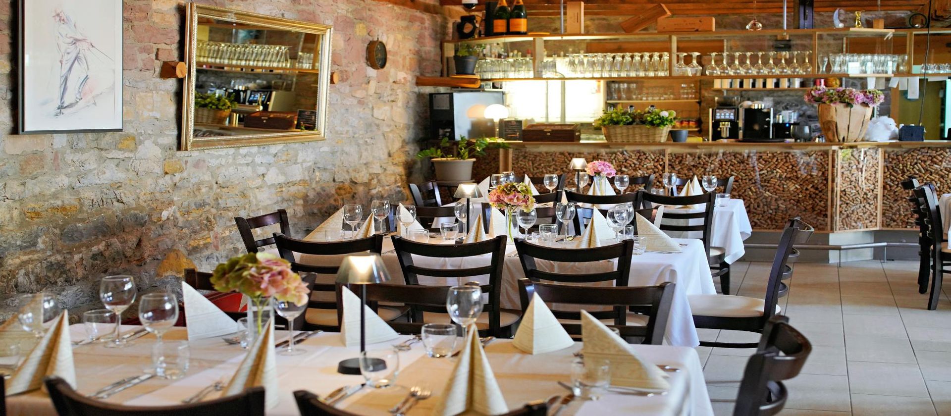 Restaurantinnenraum mit gedeckten Tischen. Steinwände, Bar und Gläser.