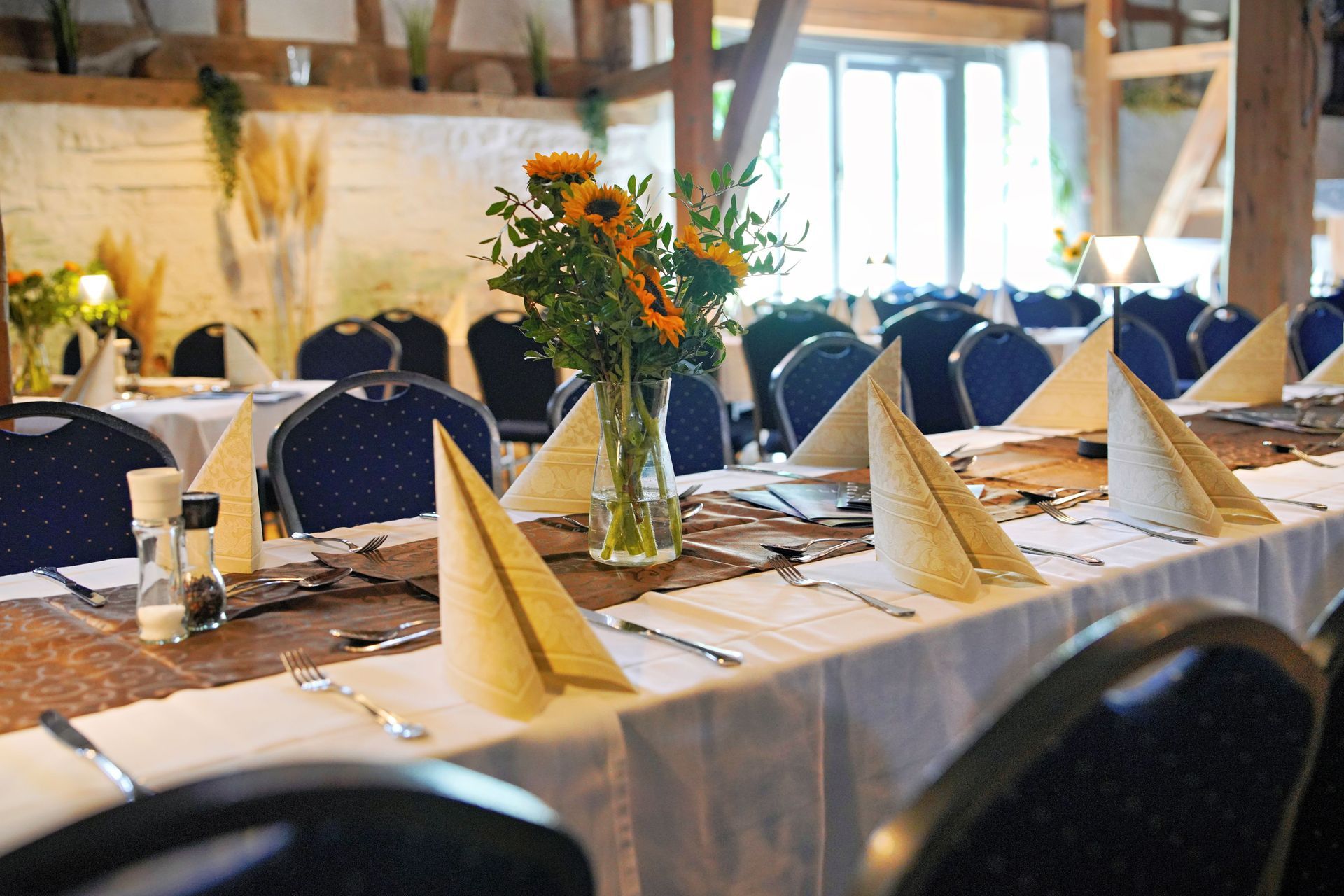 Tischgedeck mit Sonnenblumen, Speisekarten und Besteck, von oben gesehen, mit Stühlen im Hintergrund.