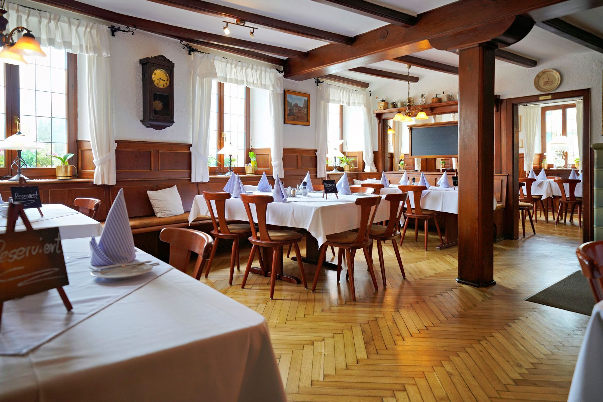 Lange, für ein Bankett gedeckte Esstische mit blauen Stühlen, weißen Tischdecken und Blumengestecken.