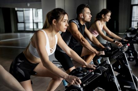 Fitnesstudio Menschen trainieren auf stationären Fahrrädern in einem Fitnessstudio und lehnen sich in einer Reihe nach vorne.