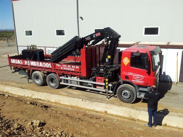 Un camión rojo con una grúa en la parte trasera está estacionado frente a un edificio.