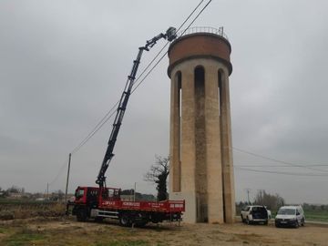 Un camión rojo con una grúa acoplada está estacionado frente a una torre de agua.