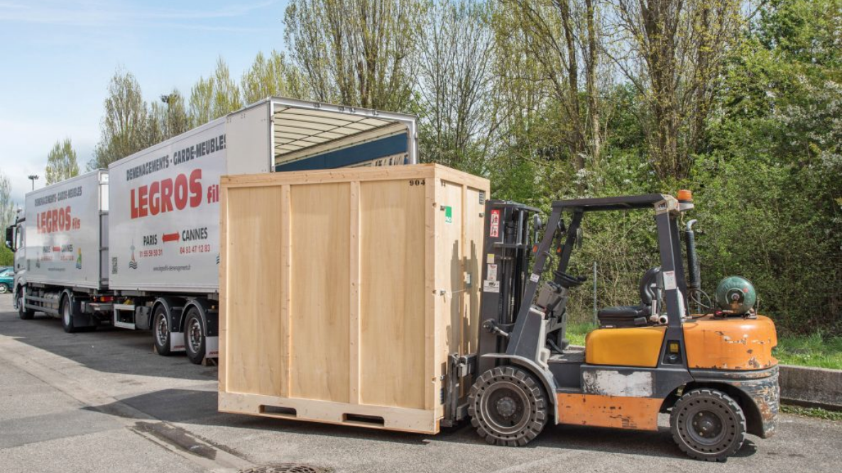 Un chariot élévateur transporte une grande caisse en bois à côté d'un camion.