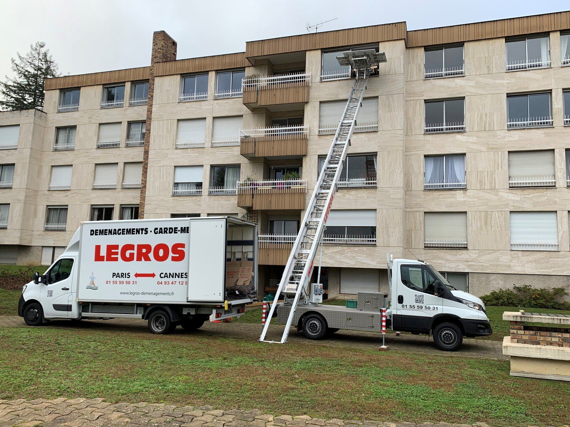 Monte-meubles installé devant un immeuble avec une camionnette blanche à côté