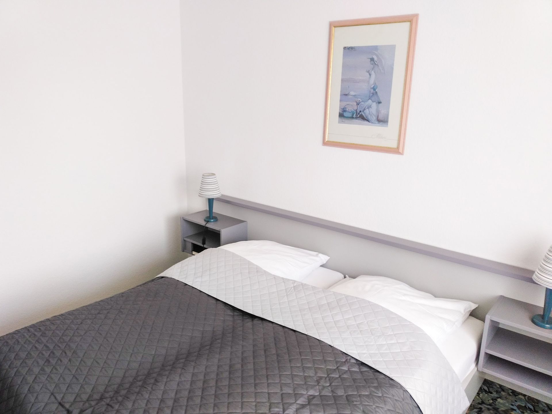 Ein Hotelzimmer mit einem Bett, einem Nachttisch, Lampen und einem Bild an der Wand.