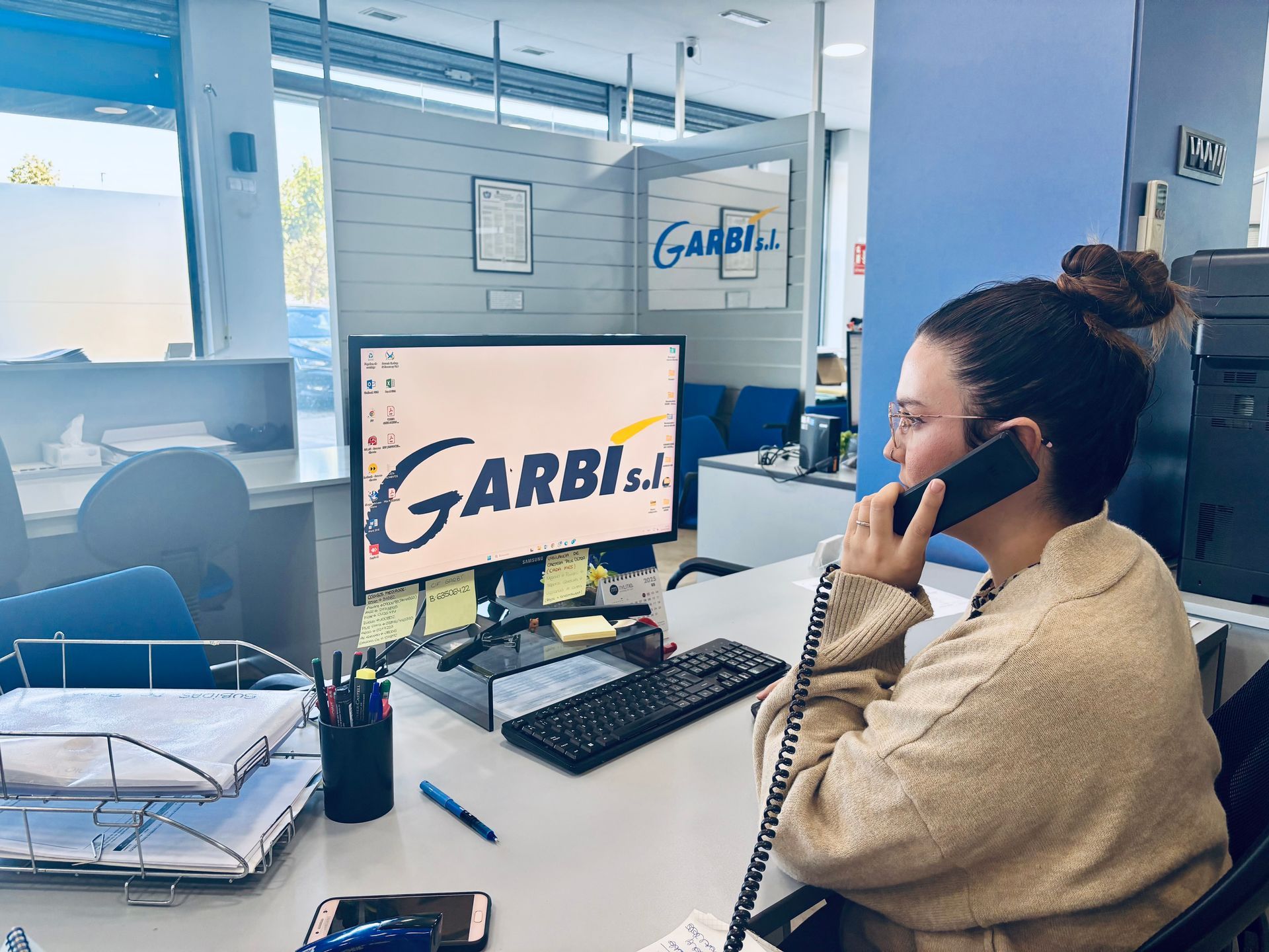 Empleada de Garbí con un teléfono fijo a la oreja mirando la pantalla de ordenador.