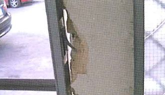 Un primer plano de una puerta mosquitera rota con un automóvil estacionado al fondo.