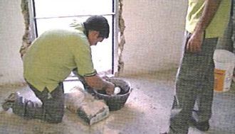 Un hombre está arrodillado junto a un cubo de cemento.