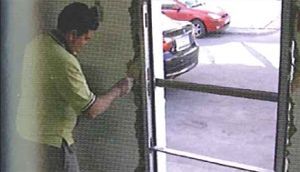 Un hombre está parado frente a una puerta con un auto rojo estacionado al fondo.