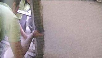 Un hombre está de pie junto a una pared sosteniendo un trozo de papel.