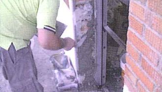 Un hombre con una camisa verde está trabajando en una pared de ladrillos.