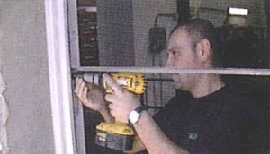 Un hombre está usando un taladro para arreglar una ventana.
