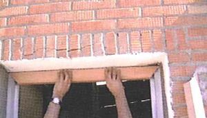 Una persona sostiene un trozo de madera frente a una pared de ladrillos.