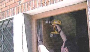 Un hombre está usando un taladro para instalar un marco de ventana.