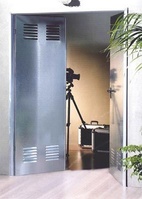 Una cámara está en un trípode en una habitación detrás de una puerta de metal.