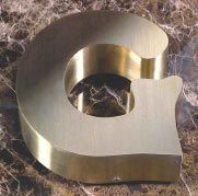 Una letra g de latón reposa sobre una superficie de mármol.