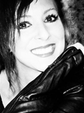 Mujer de pelo oscuro, sonriente, con maquillaje de ojos intenso, apoyada contra una chaqueta de cuero oscura.