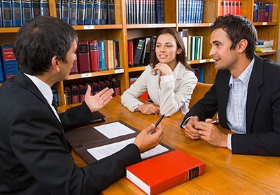 Tres personas vestidas de negocios conversando alrededor de una mesa en una biblioteca o en una oficina.