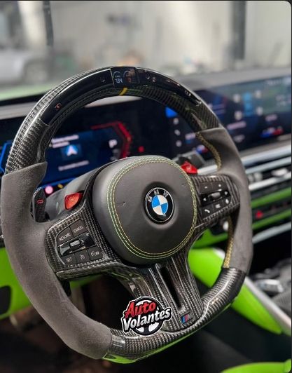 Volante BMW de fibra de carbono con empuñaduras de gamuza gris y costuras verdes.