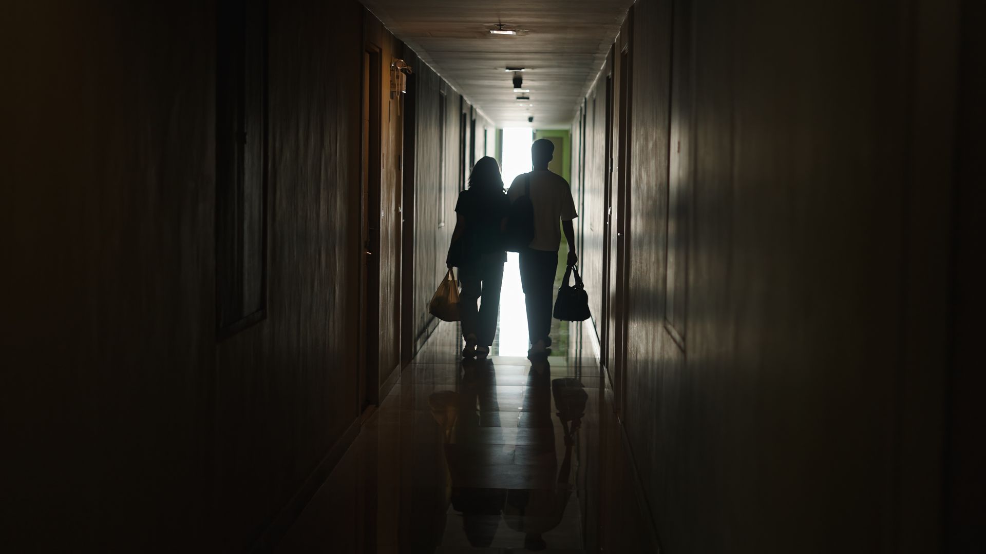 Deux silhouettes marchant dans un couloir sombre.
