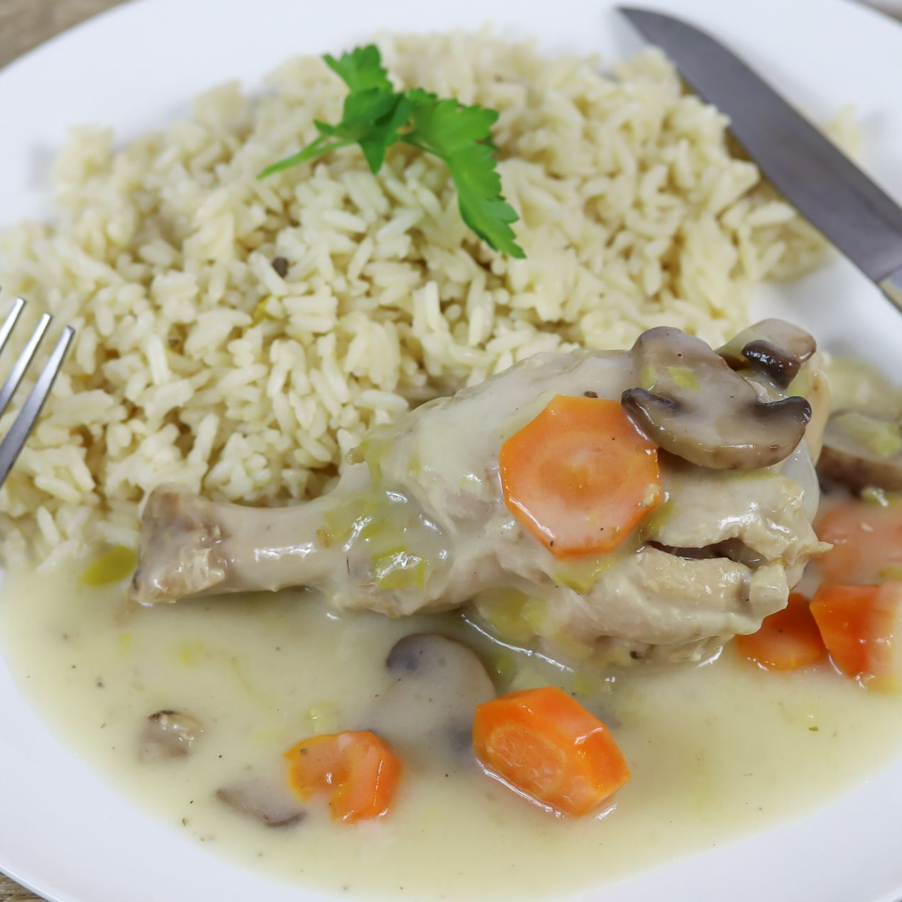 Poulet à la sauce aux champignons, carottes et riz, servi dans une assiette blanche avec une fourchette et un couteau.