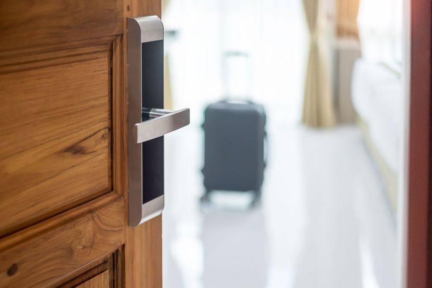Une porte en bois à poignée argentée s'ouvre sur une chambre.