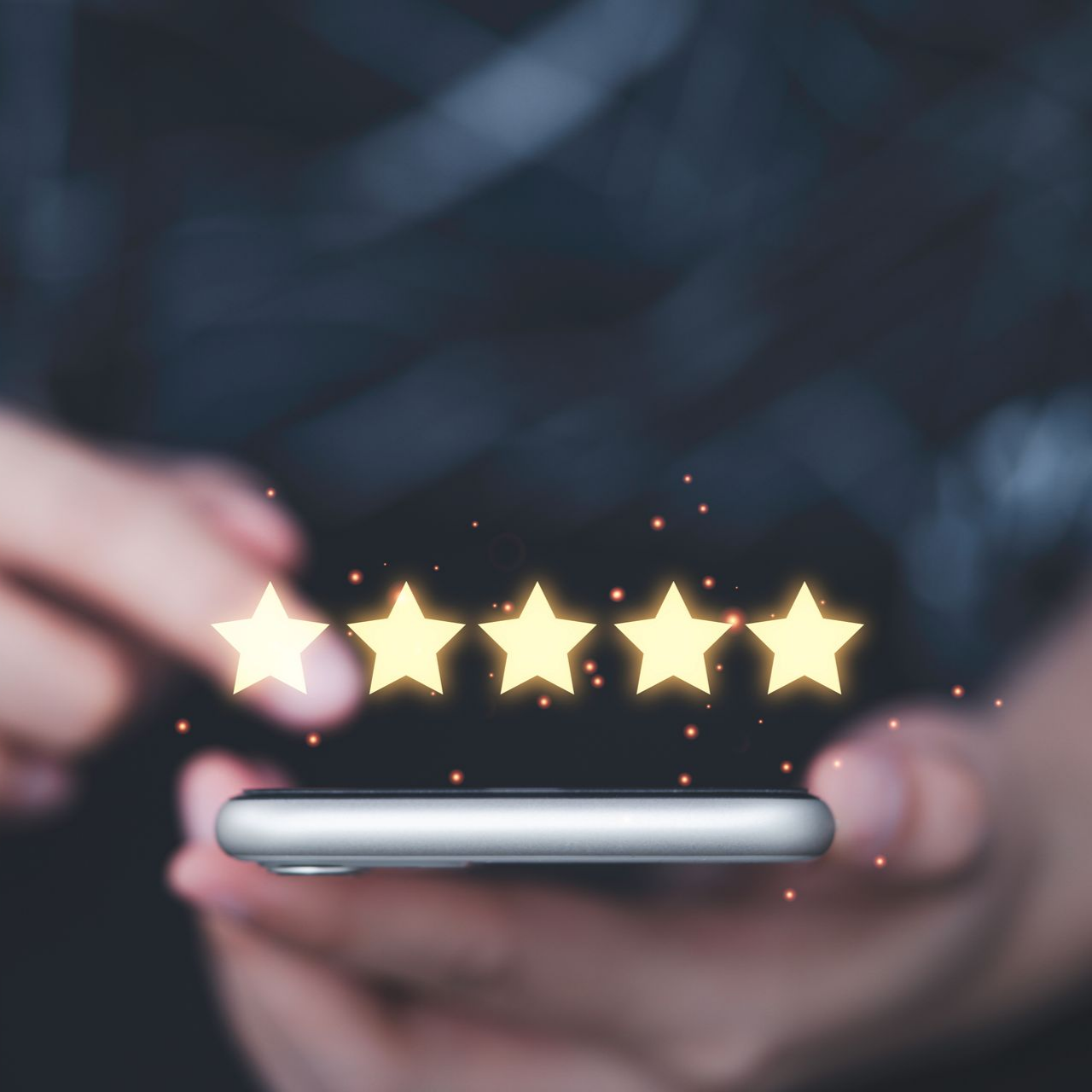 Une main tenant un smartphone avec cinq étoiles au dessus.
