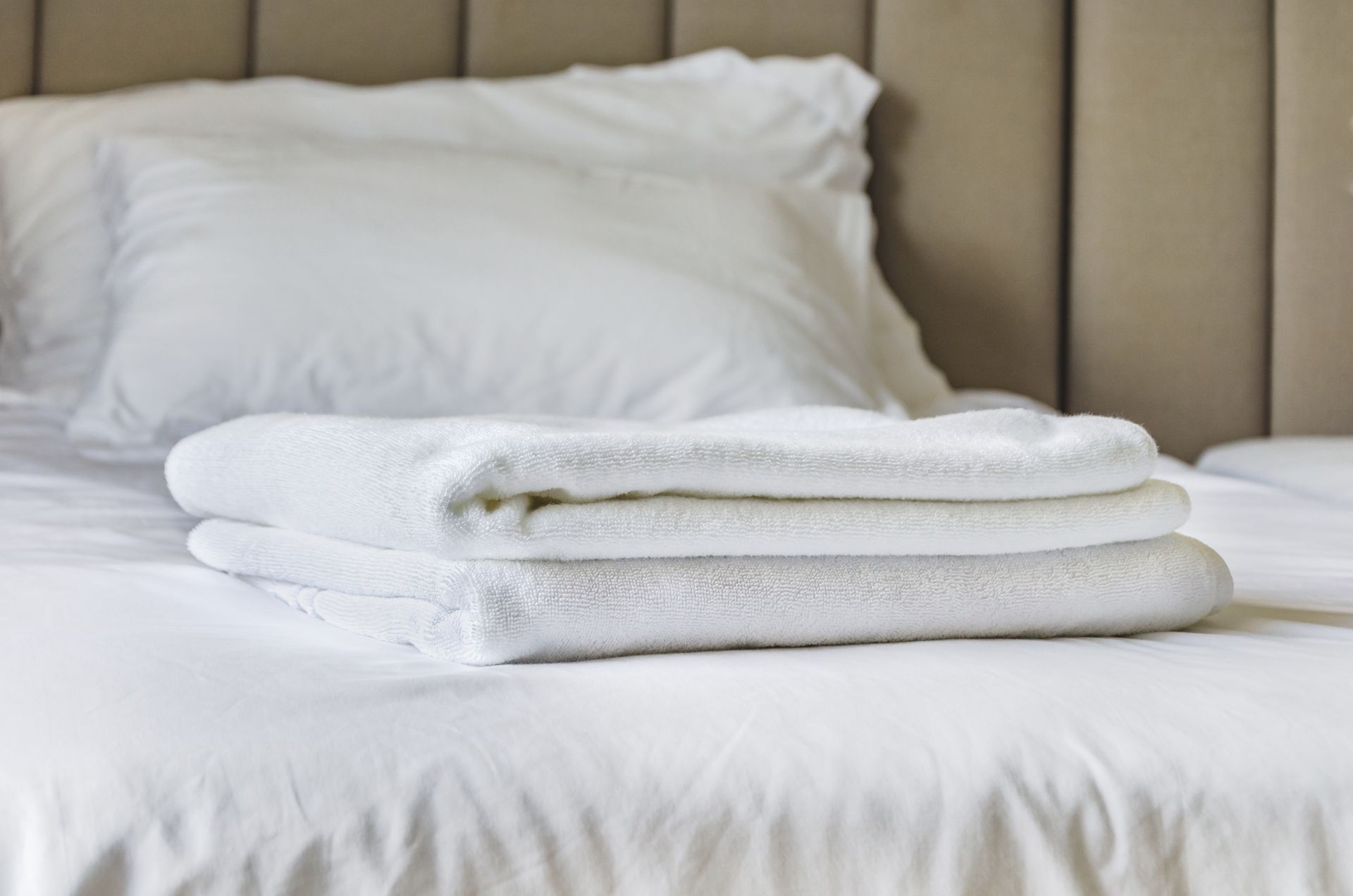 Des serviettes blanches soigneusement pliées sur un lit avec des draps et des oreillers blancs.