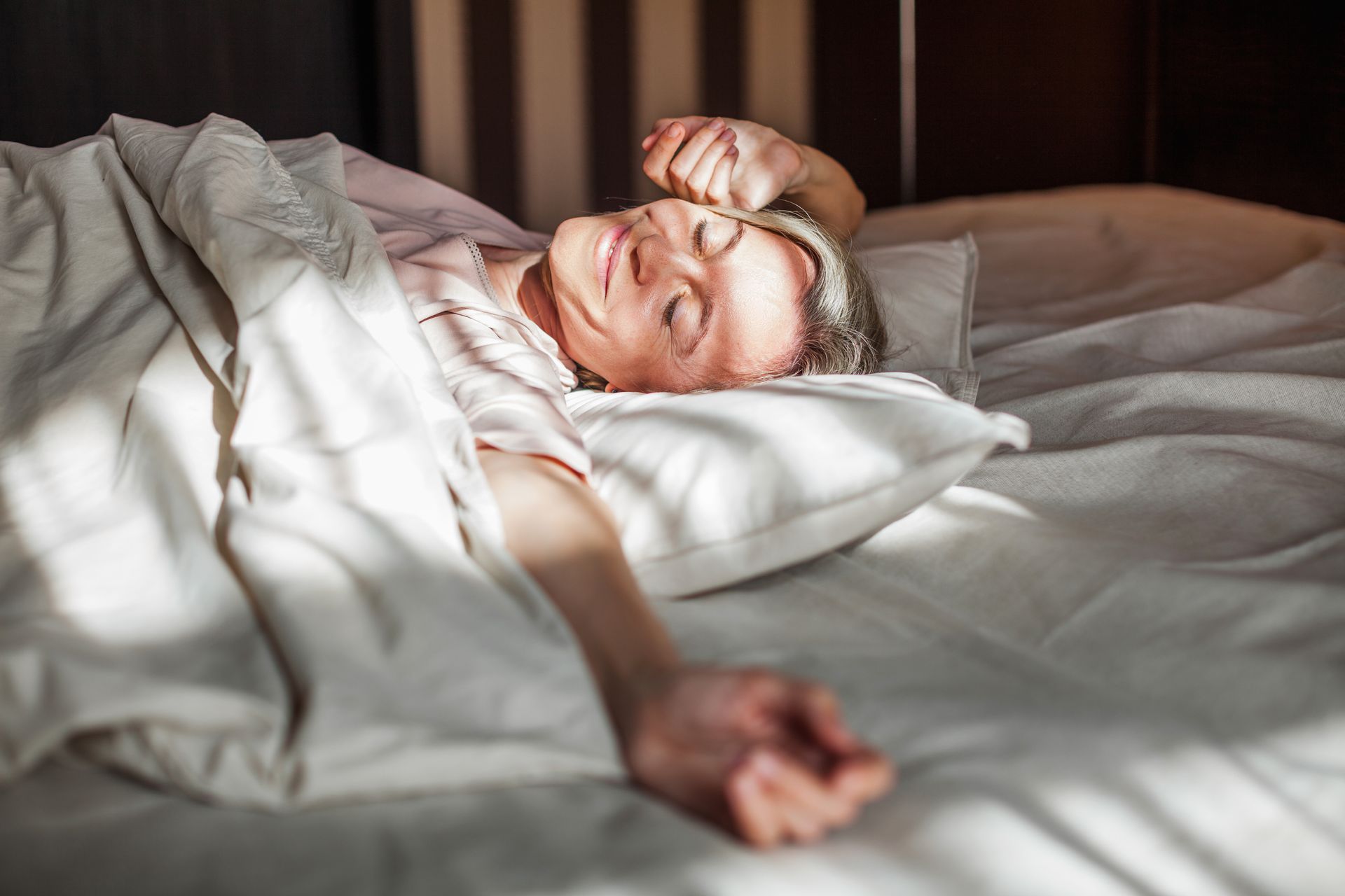 Femme dormant dans un lit dans des draps blancs.