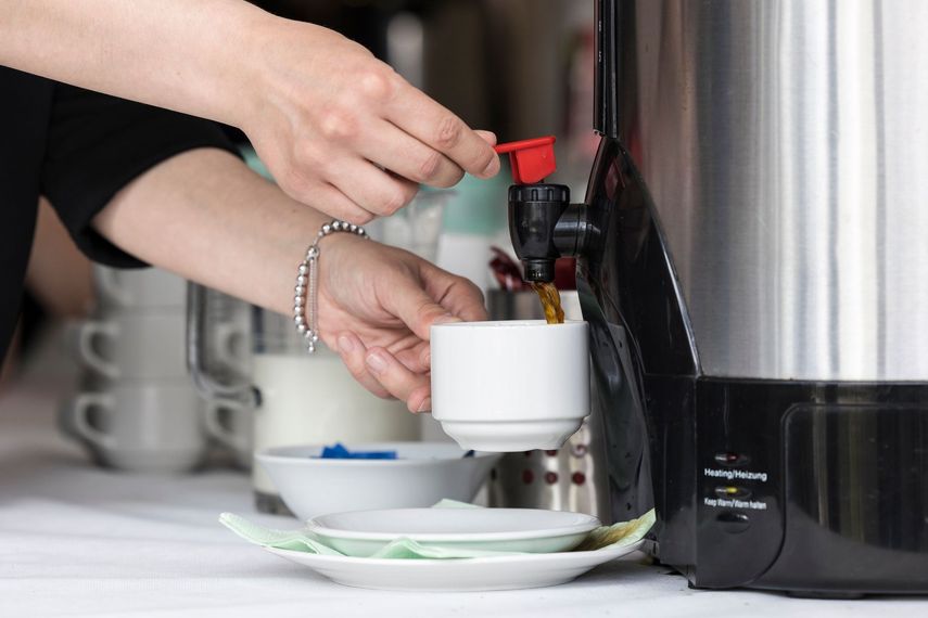 Des mains remplissent une tasse blanche à partir d'un distributeur de café.