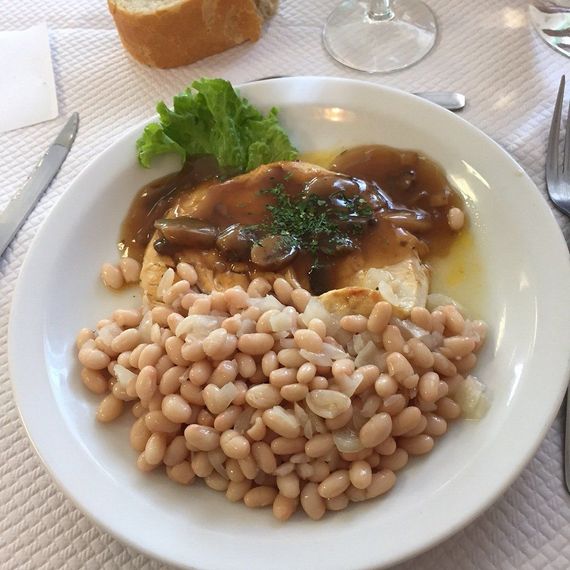 Assiette de haricots et de viande en sauce sur une table blanche, accompagnée de pain et d'un verre à proximité.