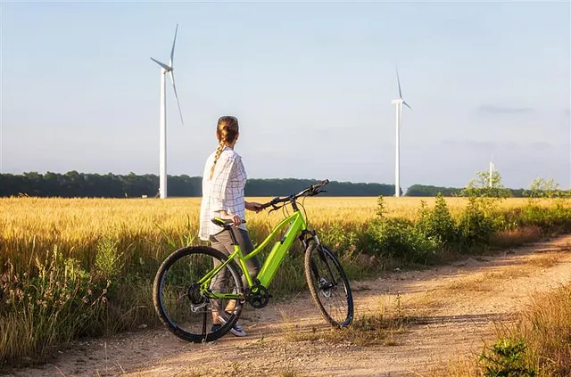 Una mujer está parada junto a una bicicleta verde en un campo con turbinas eólicas en el fondo.