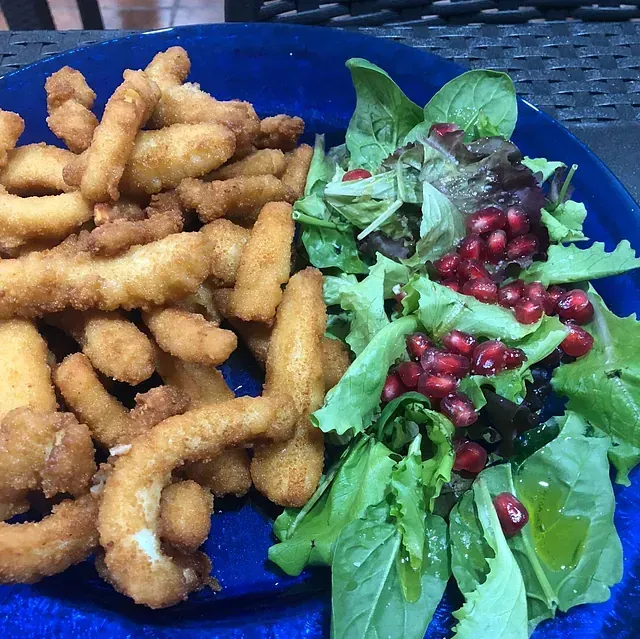 Un plato azul cubierto con comida frita y una ensalada con semillas de granada.