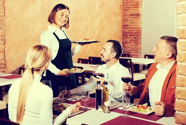 Una camarera está sirviendo comida a un grupo de personas sentadas en una mesa en un restaurante.