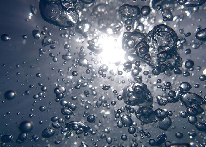 Bulles et gouttelettes scintillantes suspendues dans une eau bleue avec une lumière vive au centre