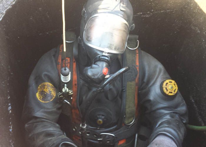 Plongeur en combinaison et casque noirs à l'intérieur d'un submersible, vu à travers une vitre mouillée.