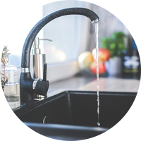 Robinet de cuisine noir laissant couler l'eau dans un évier, avec un plan de travail flou en arrière-plan.