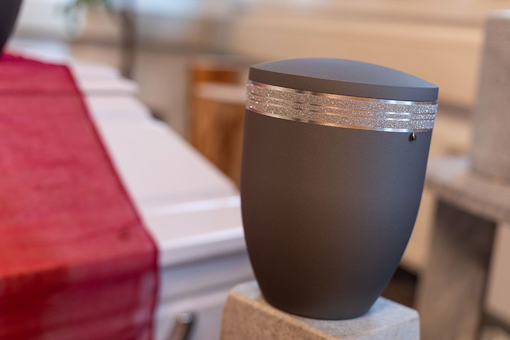 Eine schwarze Urne mit einer silbernen Schleife steht auf einem Betonblock.