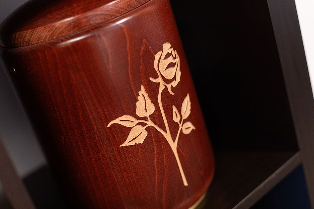 Auf einem Regal steht eine Holzurne mit einer Rose darauf.