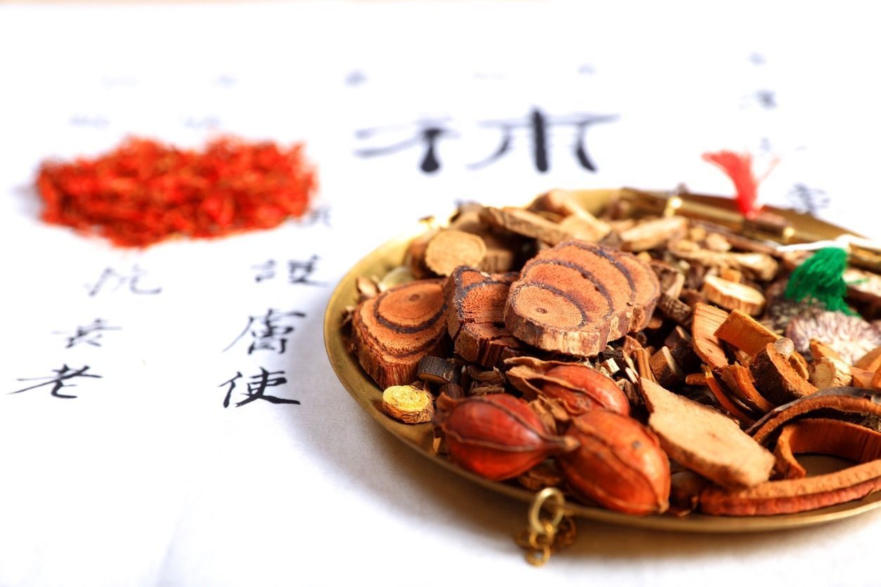 Surtido de hierbas medicinales tradicionales chinas en un recipiente dorado, con bayas rojas y caracteres escritos a mano en papel en el fondo.