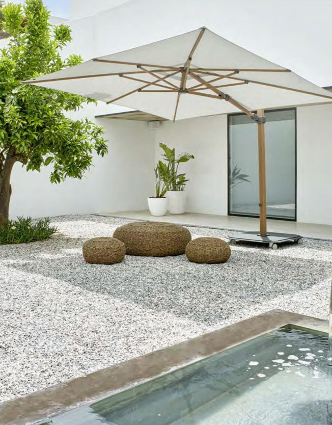 Parasol carré et petit siège d'extérieur dans un jardin avec graviers bordant une piscine
