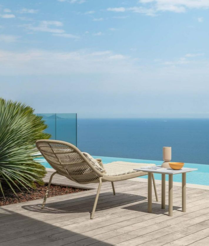 Transat et table de café couleur beige sable finition en rotin sur une terrasse bordant une piscine face à la mer