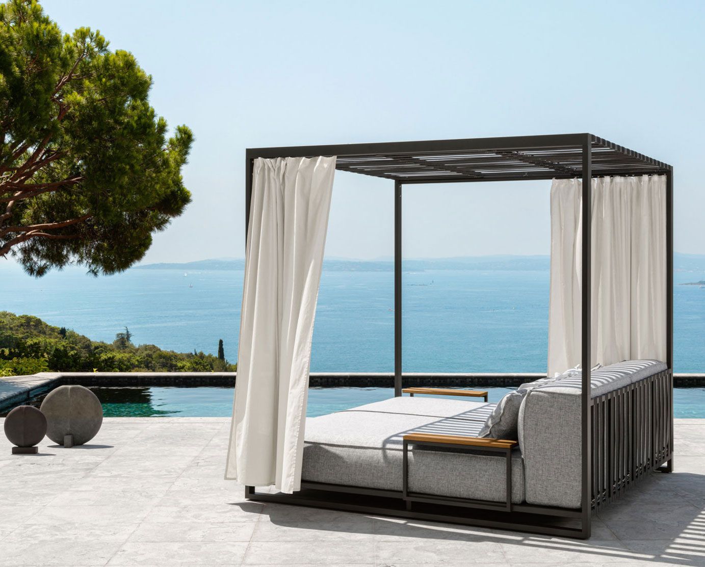 Transat style baldaquin sur une terrasse en pierre bordée d'une piscine face à la mer