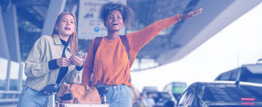 Deux jeunes personnes appelant un taxi de la main à la sortie d'un aéroport