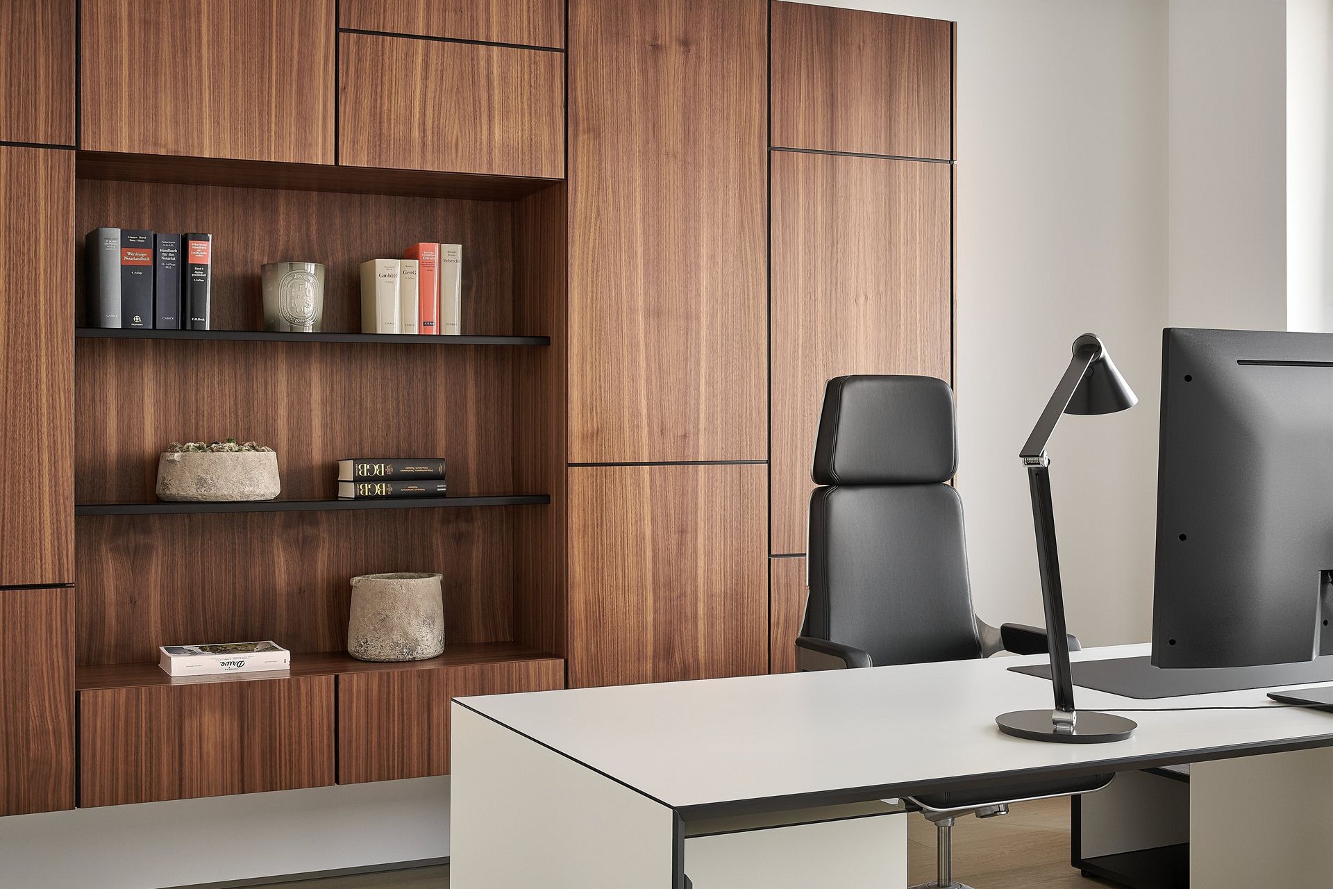 Hinter einem Schreibtisch ist ein Holz-Wandschrank mit Büchern