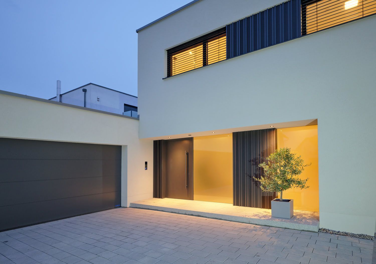 Modernes weißes Haus mit dunkler Holz-Eingangstür, warm beleuchtet